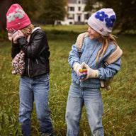 Two children in a grassy field wearing colourful kids winter hats and winter clothing.
